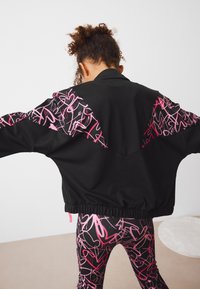 Black jacket with pink abstract patterns on sleeves, elastic hem, and relaxed fit. Paired with patterned leggings in similar colors.