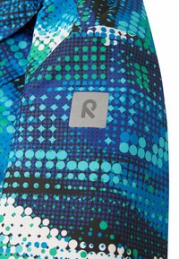 Bunt gemusterter Stoff in Blau mit verschiedenen Kreisen und Quadraten in Grün und Weiß. Verfügt über ein graues Etikett mit einem stilisierten "R"-Logo.