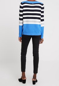 Sininen, musta ja valkoinen raidallinen neule pitkähihaisilla hihoilla, ribbitekstuuri ja selässä nappidetalji, yhdistettynä mustiin slim-fit-housuihin ja mustiin korkokenkiin.