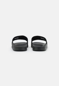 Svarta halkskydd i sandalmode med breda öppna remmar och en texturerad sula. Designen är enkel och minimalistisk, med fokus på komfort och avslappnad stil.