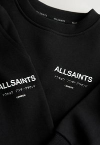 Musta ALLSAINTS-huppari valkoisella painettulla brändin nimellä, japanilaisilla merkinnöillä ja "LONDON"-tekstillä rinnassa ja hihassa.