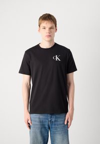 Black cotton t-shirt with short sleeves and a crew neck, featuring a small white "cK" logo on the chest. Casual design, standard fit.