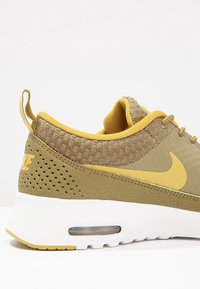 Tenisky Nike v olivově zelené a žluté barvě, vyrobené z prodyšné síťoviny a gumy, kulatá špička, polstrovaný límec a polstrovaná vzduchová jednotka v bílé podrážce.