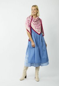 Robe rayée bleue avec broderie, associée à un châle floral rose avec une bordure rouge. Le mannequin porte des bottes à talons carrés crème.
