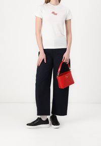 Hvid t-shirt med et rødt logo, parret med navy brede bukser, sorte sneakers og en lille rød håndtaske med en guldlås.