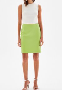 Bílý top bez rukávů spojený s přiléhavou zelenou sukni do kolen typu tužka. Tkanina působí hladce s jemným leskem. Stříbrné boty na podpatku s páskem kolem kotníku.