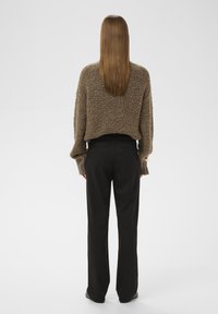 Debela smeđa pletena dukserica s krojenjem do struka i širokim rukavima, uparen s crnim hlačama ravnog kroja. Glatka tekstura, bez vidljivih uzoraka.