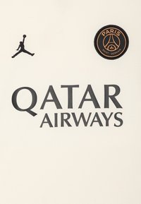 Krém színű sportmez fekete "QATAR AIRWAYS" felirattal, fekete Jumpman logóval és narancs kiemelésekkel ellátott kör alakú PSG logóval.