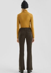 Braune Corduroy Schlaghosen mit Gesäßtaschen, kombiniert mit einem langärmeligen senfgelben Oberteil und einer schwarzen Mütze. Geschmeidige Textur und warme Farben.