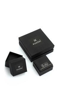 Svart pappersförpackning i set, inkluderar en stor låda med en glänsande logotyp och två mindre lådor, varav en har en varningsetikett och ett meddelande på återvunnet papper.