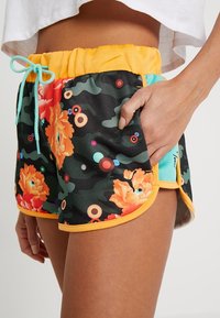Shorts à motif floral en noir, avec des accents orange et bleu sarcelle, une taille élastique, et des poches latérales. Tissu synthétique texturé.