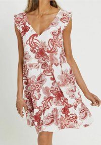 Vit klänning med röda blommönster och paisleymönster, V-ringning med volangärmar, åtsittande midja och en utsvängd kjol med ett lagerat fåll.