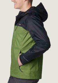 Olivengrüne und schwarze Regenjacke mit Kapuze, ausgestattet mit Reißverschlusstaschen und verstellbarem Kordelzug. Hergestellt aus wasserabweisendem Material.