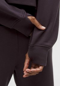 Lila Sporttop mit gerippten Bündchen und lockerer Passform. Weiche Textur mit Nahtdetails, kombiniert mit passenden, enganliegenden Hosen.