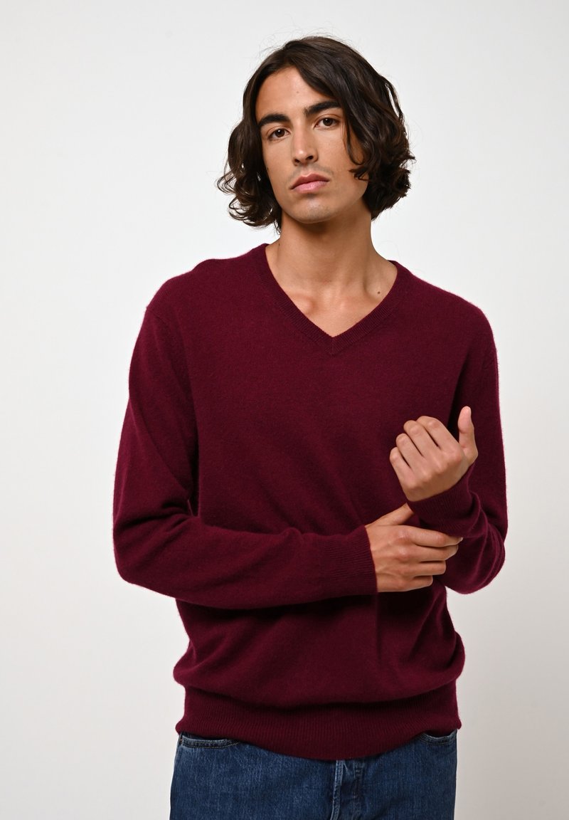 Pullover bordeaux a scollo a V realizzato in morbido tessuto, con maniche lunghe e polsini a costine, abbinato a jeans in denim blu. Design semplice e accogliente.