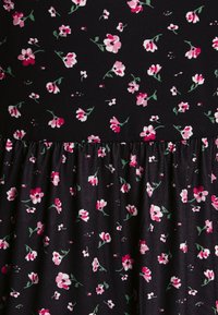 Tecido preto com pequenas flores rosas e brancas e folhas verdes, apresentando uma costura franzida que divide duas secções do padrão floral.