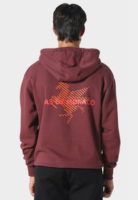 Felpa maroon con cappuccio, maniche lunghe e una grafica di un cavallo a strisce arancioni con il testo "AS DE MONACO" sotto.
