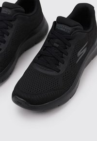 Czarne dzianinowe sneakersy z oddychającą siateczkową cholewką, płaskimi sznurowadłami, amortyzowaną podeszwą i teksturowanym wykończeniem po boku.