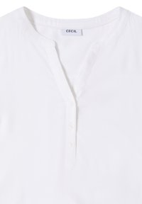 Blouse en mélange de coton blanc avec un col en V, des manches courtes et une patte de boutonnage comportant cinq boutons. L'étiquette indique "CEcil". Texture lisse.