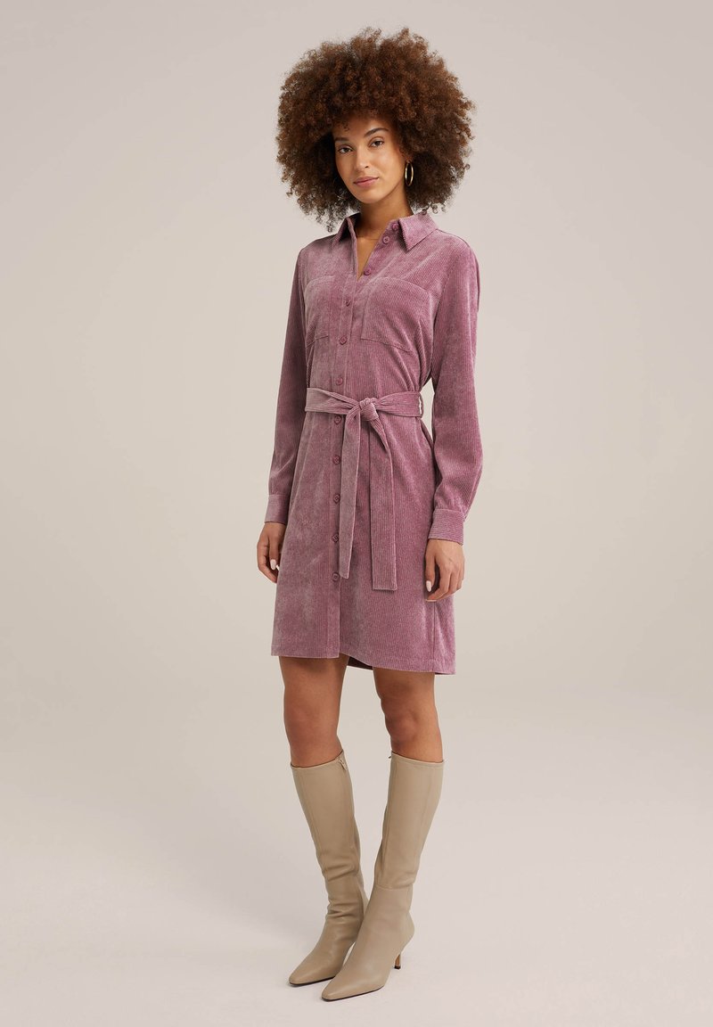 Skjortklänning i ljuslila välour med långa ärmar, knäppning och midjebälte. Stylist med knäkorta beige stövlar.
