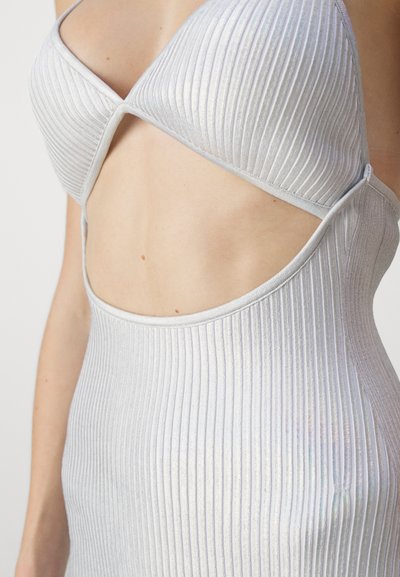Il bodysuit argento con righe presenta un design con tagli, spalline sottili e una brillantezza delicata, enfatizzando la sua silhouette aderente e la textura moderna.