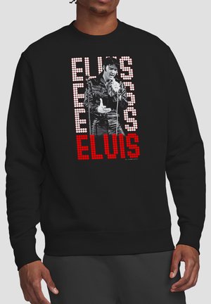 Man wearing black sweatshirt with black-and-white Elvis Presley singing, with repeated "ELVIS" text in white and red dot matrix style.