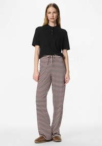 Czarna koszulka polo z krótkim rękawem i plisą na guziki, w połączeniu z szerokimi spodniami w bordowo-kremowe paski, wyposażonymi w ściągacz w talii na sznurek.