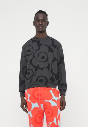 Črni pulover z veliko temno cvetlično vzorcem, z okroglim izrezom in rebrastimi manšetami, kombiniran z svetlo rdečimi in modrimi hlačami s cvetličnim potiskom.