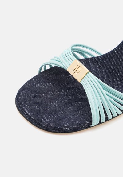 Dark blue fabric sandal with light blue twisted straps and a gold metal accent logo on the side. Smooth texture, open-toe design.