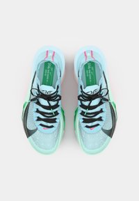 Světle modré sportovní boty s černými tkaničkami, texturovaným svrškem, zelenými akcenty a výrazným černým logem Swoosh. Gumové podrážky s růžovým detailem.