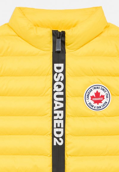 Yellow quilted jacket with black zipper labeled "DSQUARED2" and circular patch with red maple leaf and text on the chest.