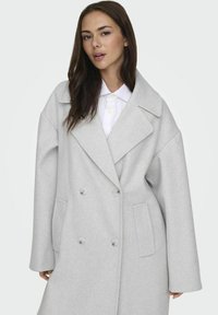 Cappotto grigio chiaro in misto lana con chiusura doppiopetto, rever a punta, fitting oversize e tasche laterali. Tessuto liscio e texture.