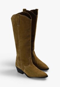 Botas de vaquero de ante marrón con punta afilada y un tacón bajo, con costuras blancas y lengüetas en la parte superior para facilitar su uso.
