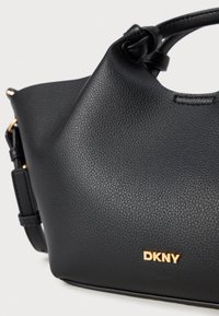 Musta nahkabag, jossa on tekstuuripinta, jossa on kultainen "DKNY"-logo. Sisältää lyhyen kahvan ja säädettävän olkahihnan.