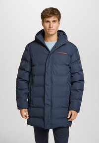 Cappotto imbottito blu navy con cappuccio, dotato di tasche con zip, polsini elasticizzati e chiusura frontale con bottoni a pressione. Accento rosso sul petto.