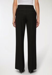 Czarne spodnie szerokie w nogawkach o dopasowanym kroju, z tylnymi kieszeniami i gładką teksturą. Projekt zawiera szlufki na pasek oraz zamek błyskawiczny.