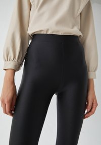 Zwarte legging van een gladde, rekbare stof met een hoge taille. Het oppervlak is strak zonder zichtbare naden of patronen.