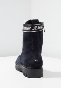 Námornické semišové kotníkové boty s černým textilním límcem se textem "TOMMY JEANS", stříbrným zipem a texturovanou gumovou podrážkou.