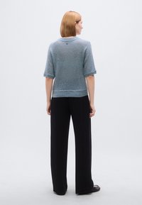 Πουλόβερ από απαλό, ανοιχτό μπλε πλεκτό με κοντά μανίκια και στρογγυλή λαιμόκοψη. Συνδυασμένο με φαρδιά μαύρη παντελόνα. Απλός σχεδιασμός, διακριτή υφή.