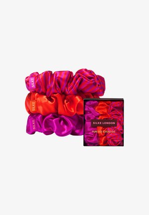 Drei Seidenscrunchies in Rot, Pink und Magenta, eines davon mit gestreiftem Muster. Verpackt in einer schwarzen Schachtel mit einem vorderen Etikett.