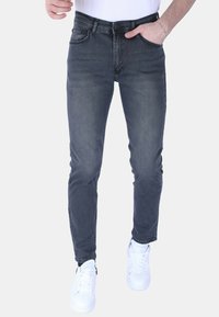 Slim-fit donkergrijze jeans met een gladde textuur, vijf zakken en een rits, gecombineerd met witte sneakers voor contrast.
