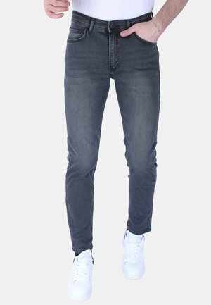 Slim-fit donkergrijze jeans met een gladde textuur, vijf zakken en een rits, gecombineerd met witte sneakers voor contrast.