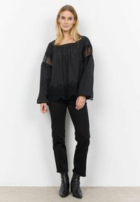Sort langærmet bluse med blonder detaljer på ærmer og kant, med en bred udskæring og løst fit, parret med sorte slim-fit bukser og ankelstøvler.