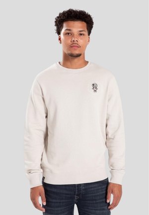 Light beige sweatshirt made of soft fabric, featuring a round neckline and ribbed cuffs. Small graphic logo on the chest.