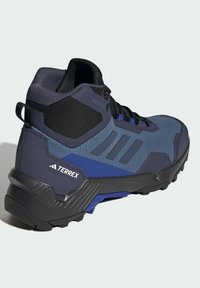 Blå och mörkgrå hög sko för vandring med texturerad mesh-övre del, förstärkt tåhätta, framträdande mönstrad sula och Terrex-logotyp.