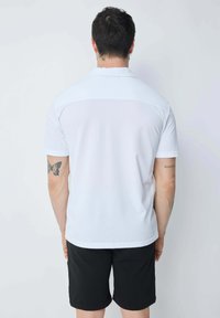Polo shirt blanc en tissu lisse, à manches courtes, avec un panneau contrasté à l'arrière, associé à un short noir.