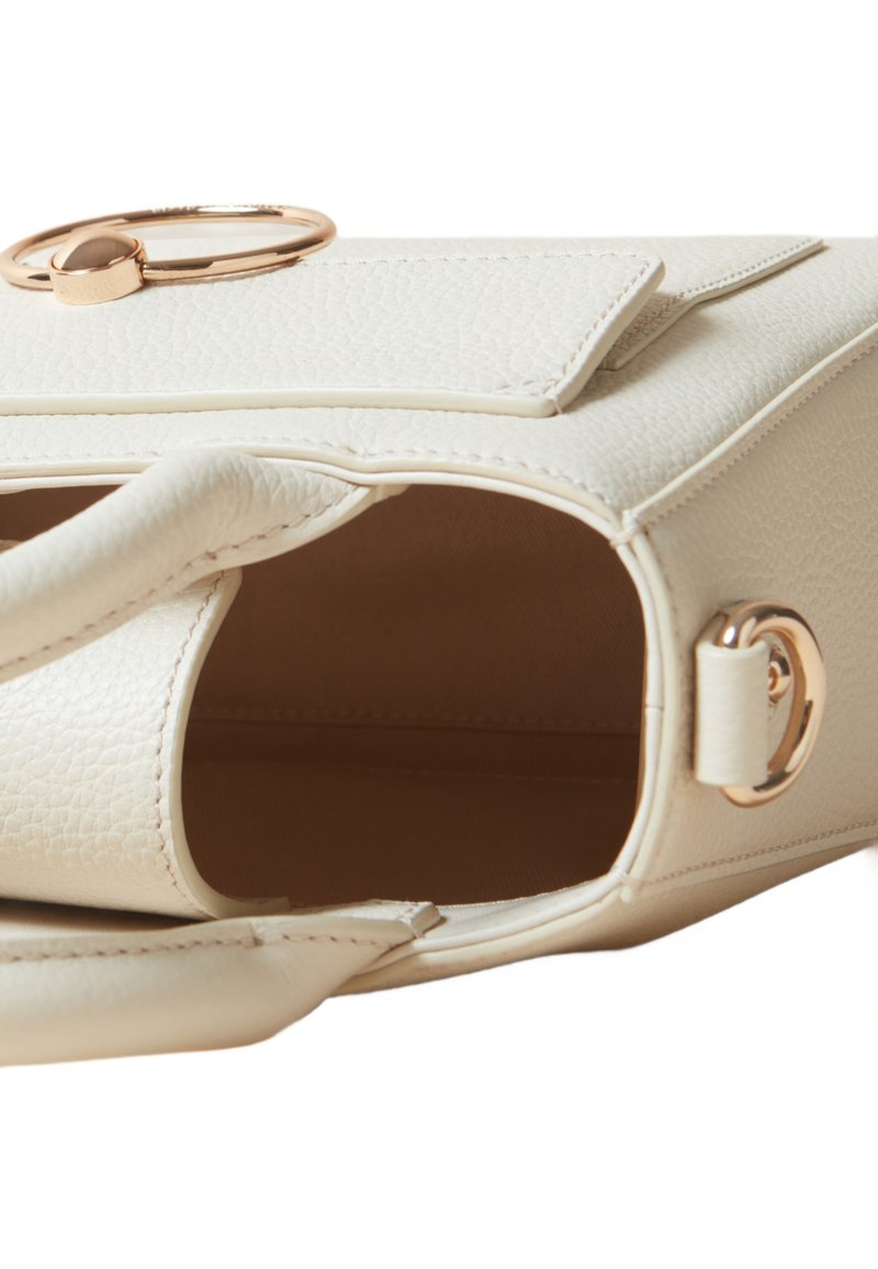 Sac à main texturé blanc avec un haut plat, un accent circulaire doré et un intérieur ouvert. Dispose d'une courte poignée et de quincaillerie dorée.