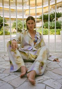 Multikleurige satijnen loungewear-set met een blouse met knopen en wijde broek, met een zachte, glanzende textuur, die pastelkleurige paarse en gele tinten mengt.