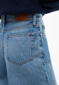 Гръб на светлосини дънки с малко лого Tommy Hilfiger на задния джоб и кафява кожена маркова лепенка на колана.