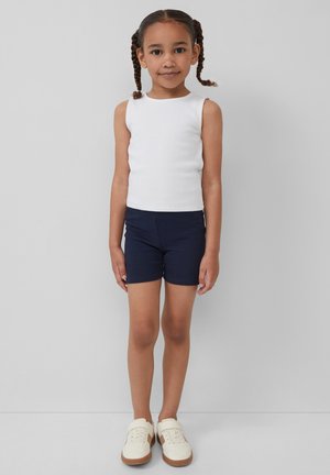 Weißes geripptes Tanktop, marineblaue Shorts und cremefarbene Sneakers. Das Outfit weist ein einfaches, tailliertes Design auf, das sich gut für die Freizeit eignet.
